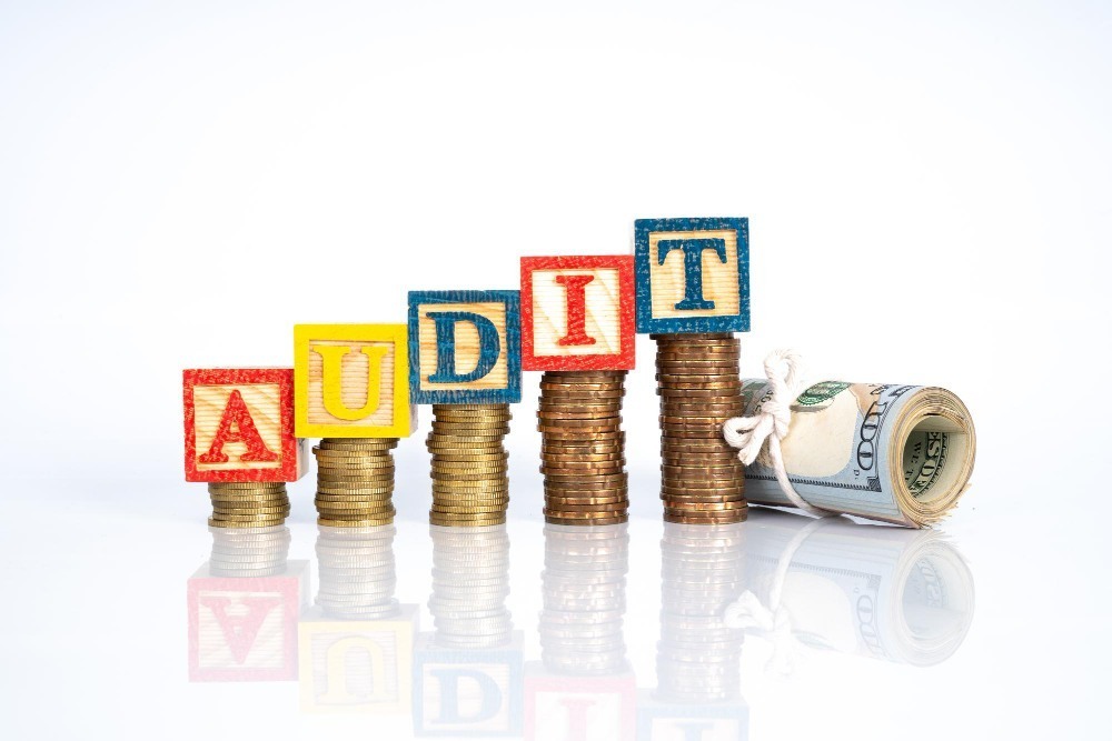 Audit concept showing stacked coins with audit blocks and rolled dollar bill